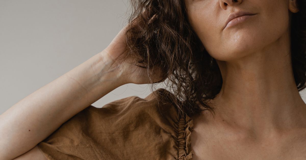 can-you-start-faceless-marketing-with-no-experience Woman looking up with hand in hair, wearing a brown linen top, face not fully visible — faceless content creator aesthetic.