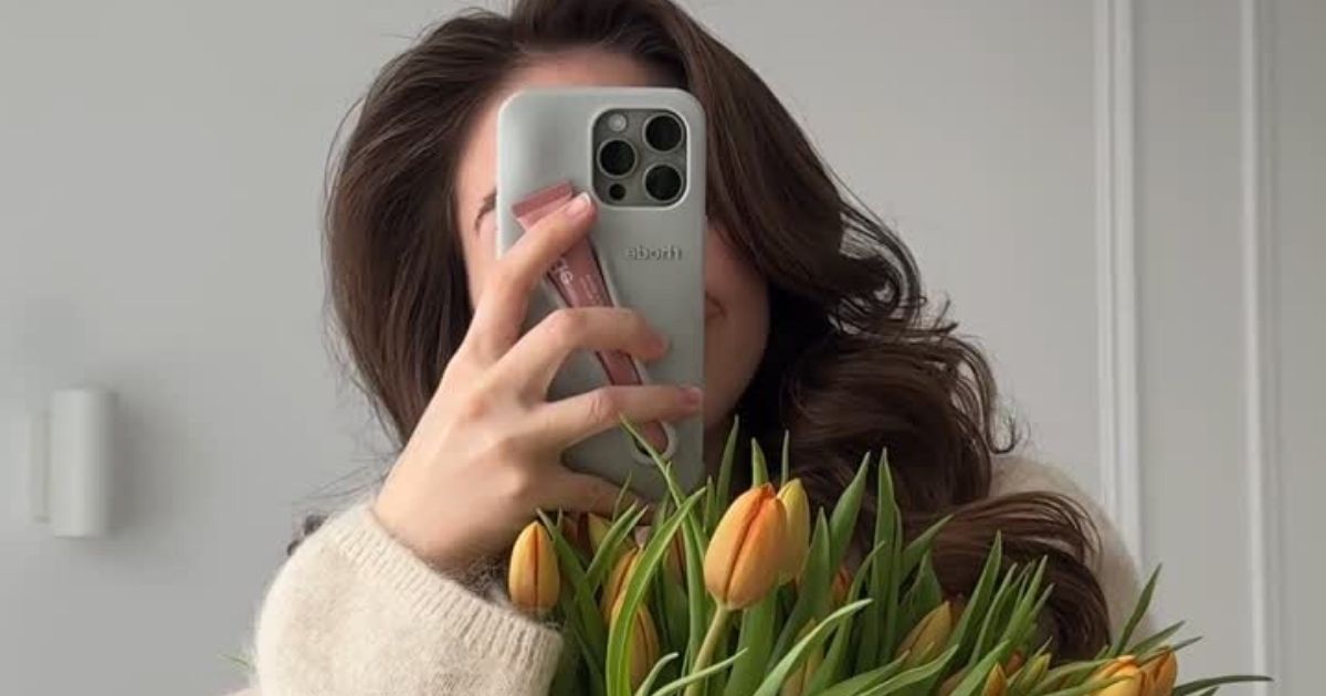 how-to-start-a-faceless-page Image of abrunette woman holding tulips and behind her phone demonstrating faceless Instagram.